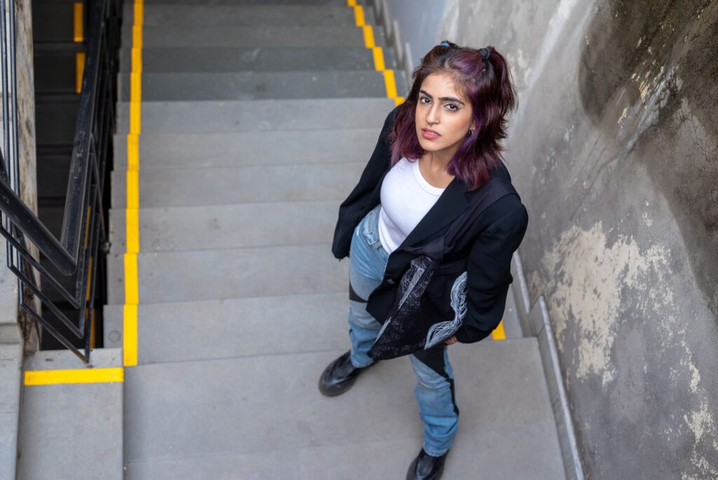 Woman in urban stairwell, casual attire, looking up with confident expression.
