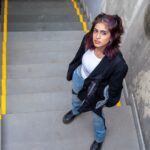 Woman in urban stairwell, casual attire, looking up with confident expression.