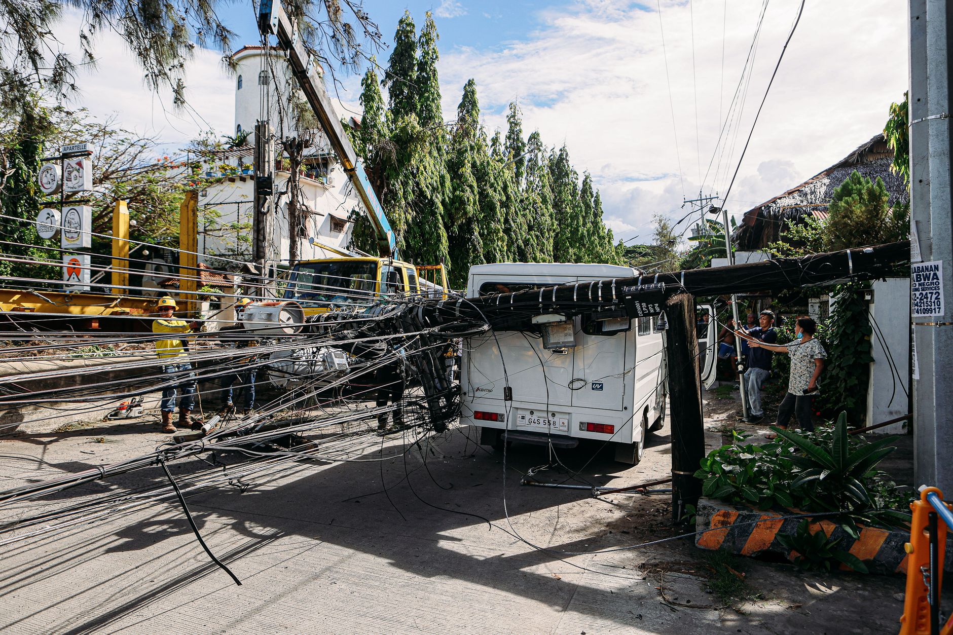 Utility crew working on damaged power lines after accident on a city street with a white van involved.