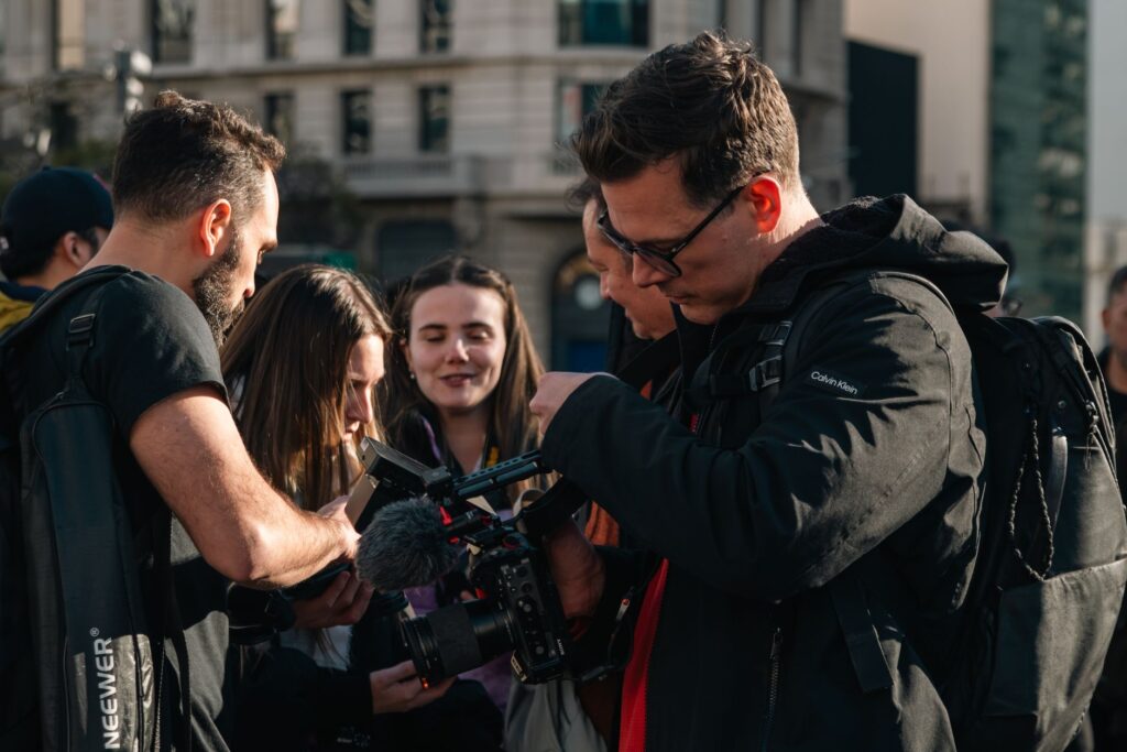 A diverse group of filmmakers collaborates outdoors, reviewing footage on a professional camera.