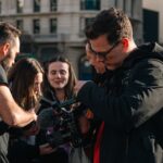 A diverse group of filmmakers collaborates outdoors, reviewing footage on a professional camera.