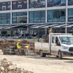 Workers unloading materials from a truck at a construction site in front of a car dealership.