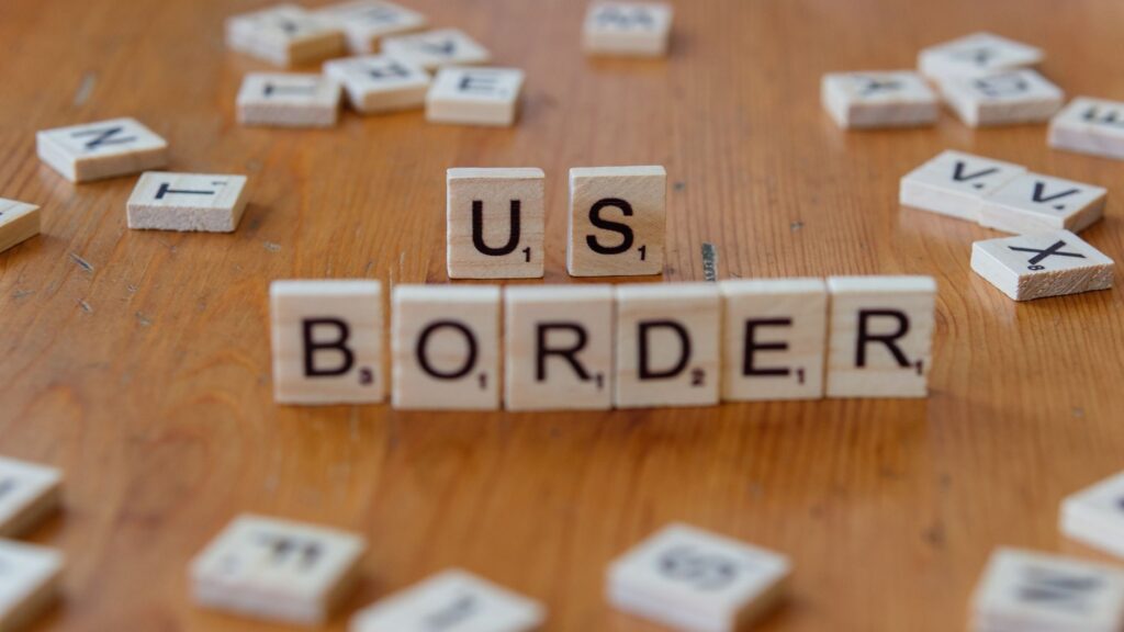 Scrabble tiles spelling 'US Border' on a wooden surface, symbolizing immigration themes.