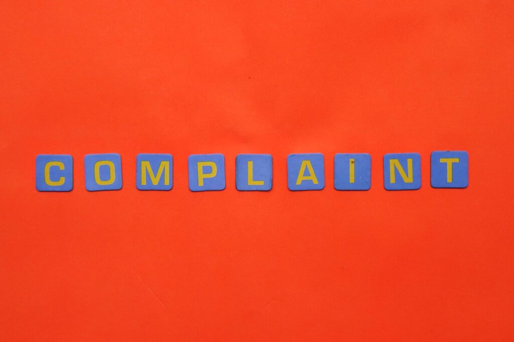 Blue letter tiles spelling 'COMPLAINT' on a vibrant red surface.