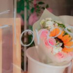 A vibrant bouquet of flowers behind a glass with 'Flores' written on it, softly lit.