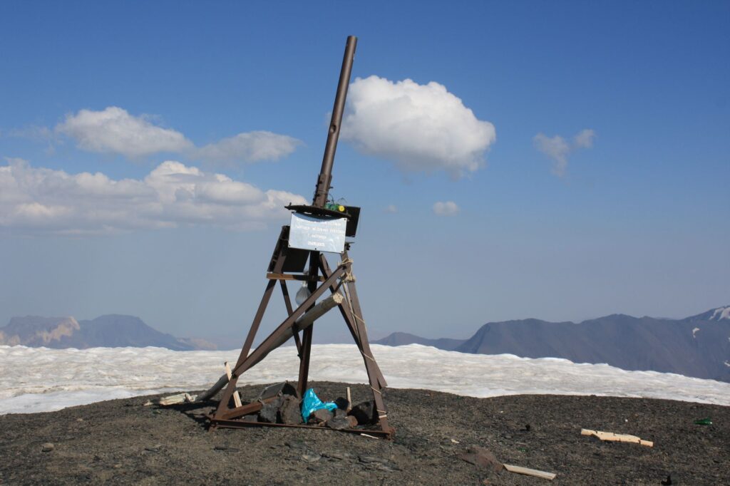 A wooden tripod structure atop a snowy mountain with clear blue skies.