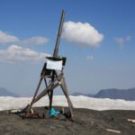 A wooden tripod structure atop a snowy mountain with clear blue skies.