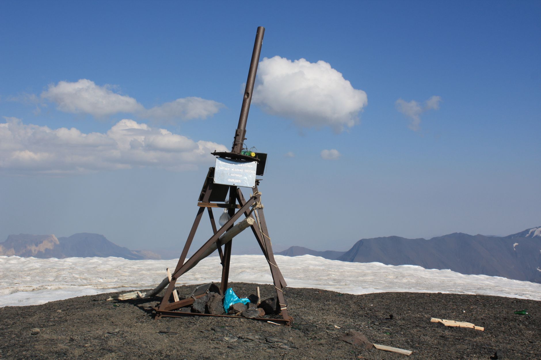 A wooden tripod structure atop a snowy mountain with clear blue skies.