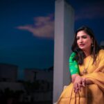 Portrait of an Indian woman in a yellow sari, seated with a serene expression outdoors during twilight.
