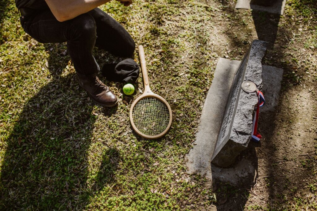 A solemn scene of a fallen tennis player memorialized with a racket and ball at a grave.
