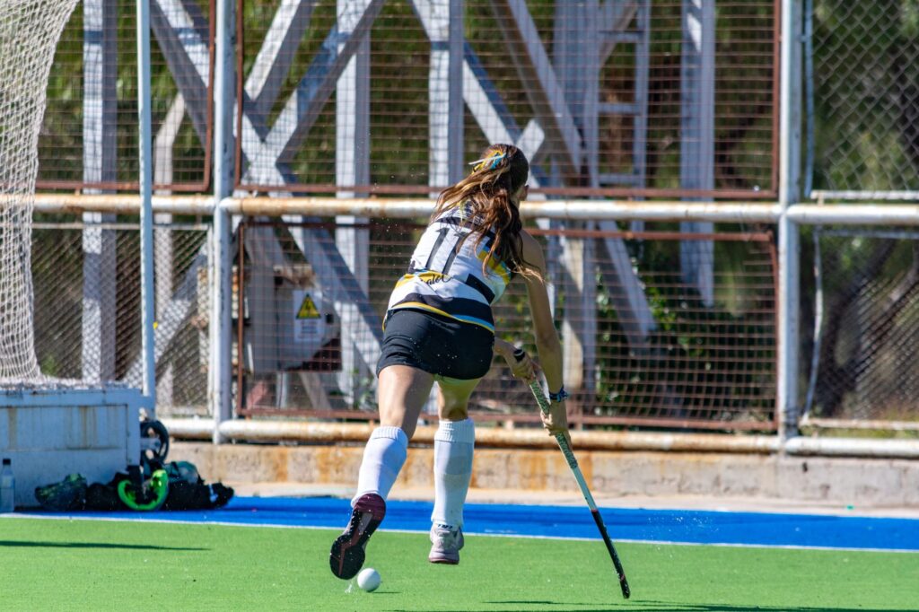 Female field hockey player running with the ball on a sunny day on the field.