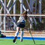 Female field hockey player running with the ball on a sunny day on the field.