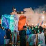 Vivid night-time celebration in France with crowds waving flags in city square.