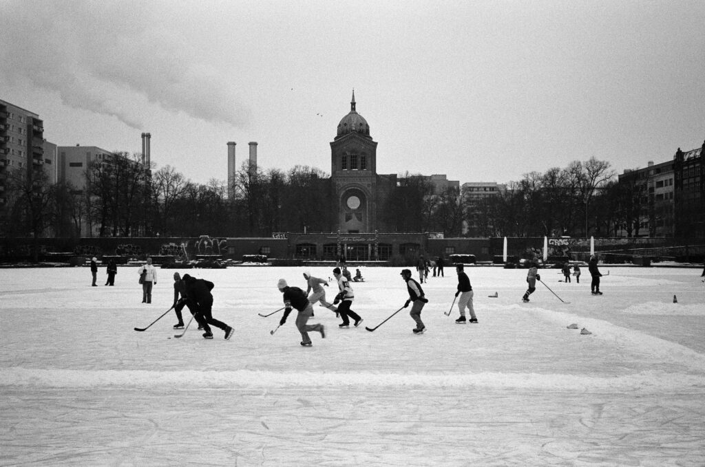 A black and white photo of people playing ice hockey near a landmark in Berlin.