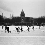 A black and white photo of people playing ice hockey near a landmark in Berlin.