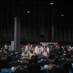 Indoor chess tournament with diverse participants gathering around tables.