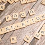 Wooden scrabble tiles arrange to spell 'Food Inflation' on a rustic wooden surface, conceptually depicting rising food prices.