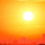 A city skyline silhouetted against a vivid, orange sunset sky.