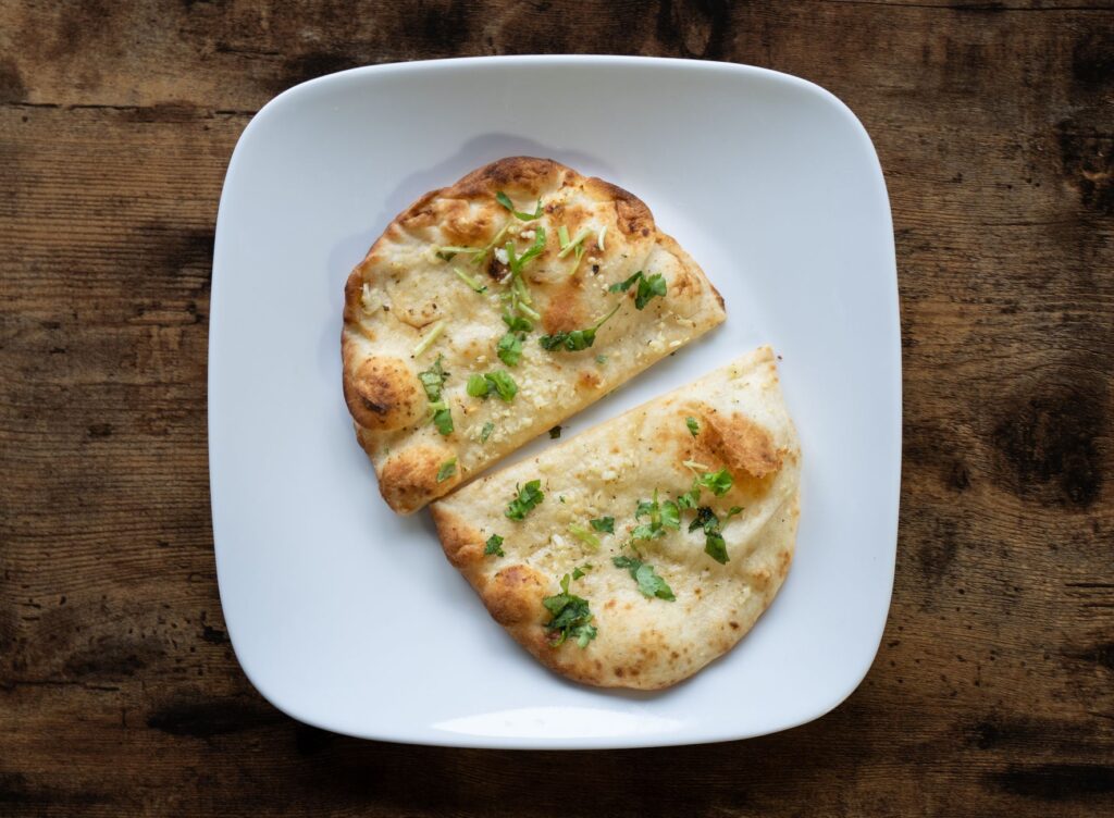 Appetizing garlic naan bread on a white plate, garnished with herbs.
