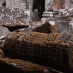 Close-up of moss-covered stone ruins at Angkor site in Cambodia, showcasing intricate ancient carvings.