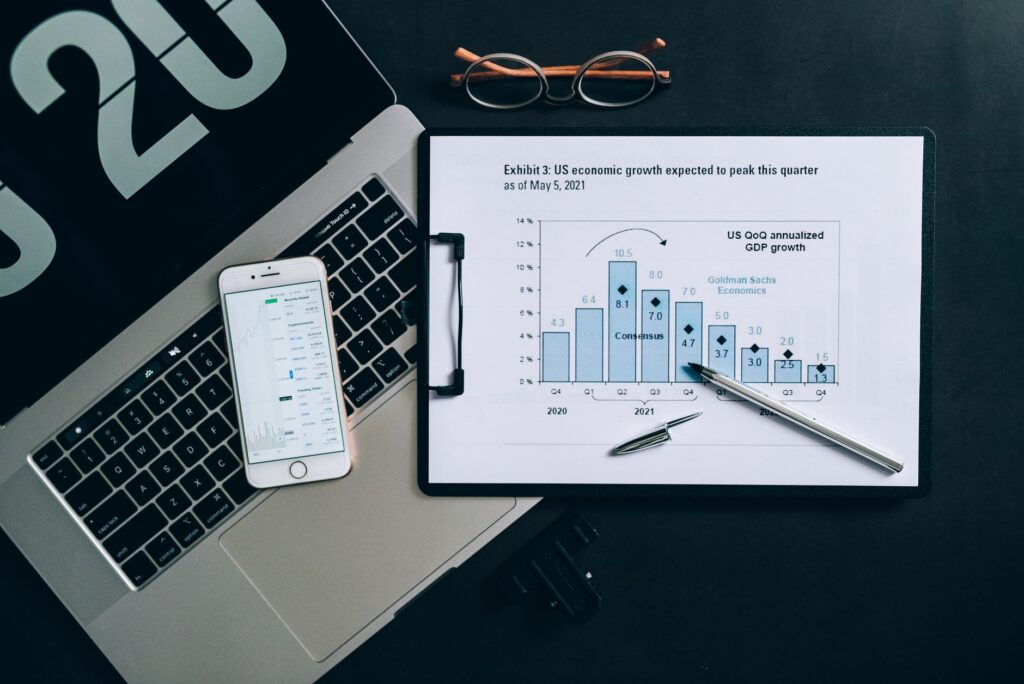 Top view of a financial data analysis setup with laptop, smartphone, and graph on clipboard.