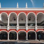Elegant colonial-style building with red and white arches and clear blue sky.