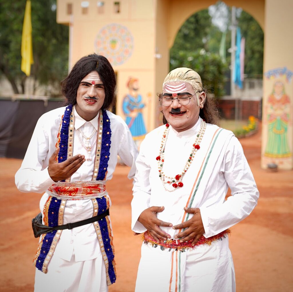 Two men in traditional Indian attire and masks celebrate a cultural festival outdoors.