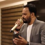 South Asian male singing passionately in an indoor venue in Ahmedabad, India.