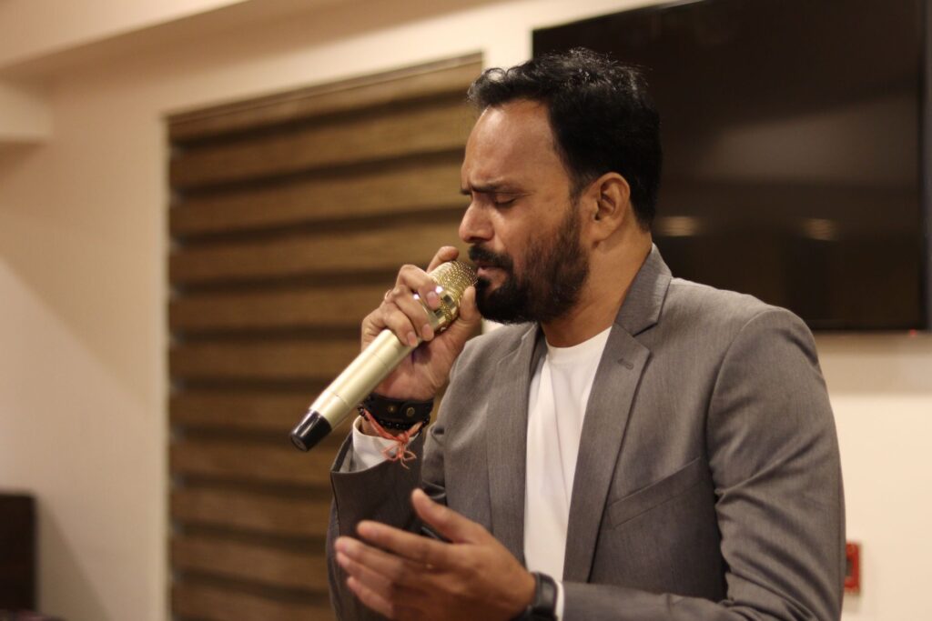 South Asian male singing passionately in an indoor venue in Ahmedabad, India.