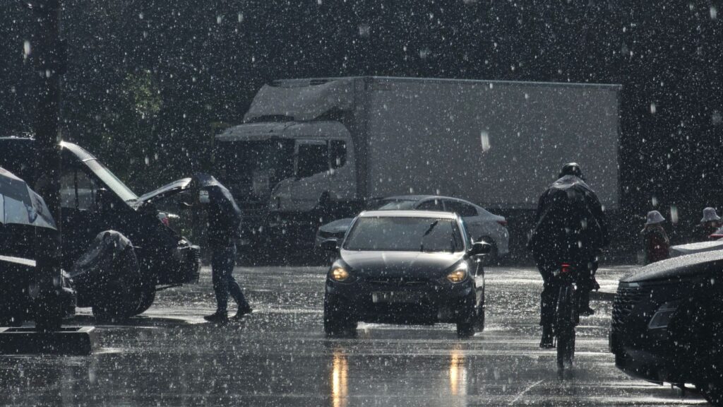 Moody urban street scene in heavy rain with cars and pedestrians.