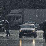 Moody urban street scene in heavy rain with cars and pedestrians.