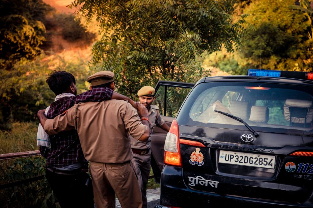 Police officers assist an individual into a patrol car outdoors during daytime.