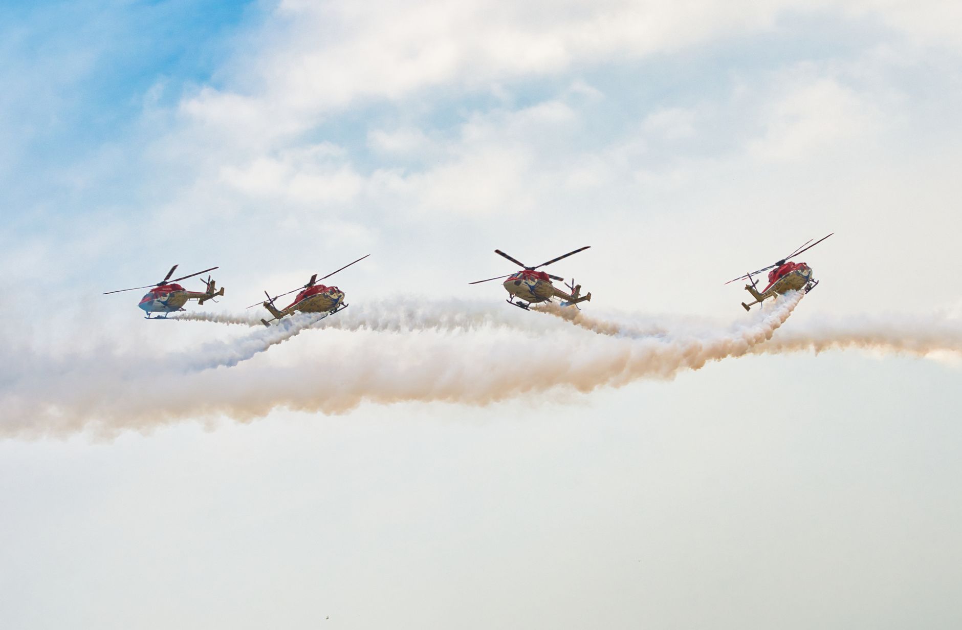 Four helicopters perform synchronized aerobatics with smoke trails in the sky.