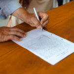 Close-up of a person signing a document on a wooden table, emphasizing detail and focus.