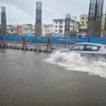 A car navigates a flooded street in Kolkata, India after heavy rain, showcasing urban challenges.