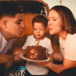 A family celebrating a child's second birthday outdoors with a cake.