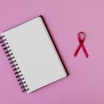 Open spiral notebook with pink breast cancer awareness ribbon on a pink background, offering copy space.