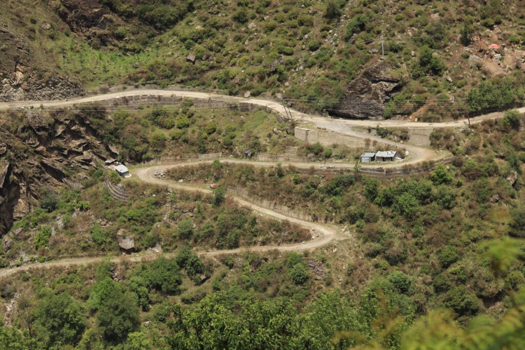 Aerial view of a winding rural road through lush green mountains in Lapas, India.