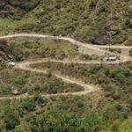 Aerial view of a winding rural road through lush green mountains in Lapas, India.