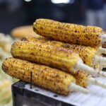 Close-up of freshly grilled corn cobs stacked in an outdoor street market setting.