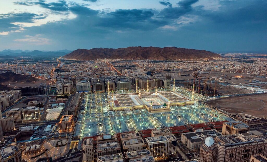 A stunning aerial view of Al-Masjid an-Nabawi in Medina at dusk, showcasing its illuminated grandeur.
