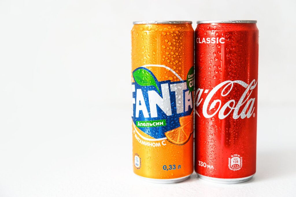 Close-up image of refreshing Coca-Cola and Fanta cans with water droplets.