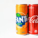 Close-up image of refreshing Coca-Cola and Fanta cans with water droplets.