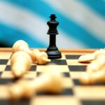 Close-up of a black king chess piece standing on a board surrounded by fallen white pieces.