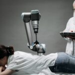 A woman receives a robotic massage as a scientist monitors, showcasing modern technology.