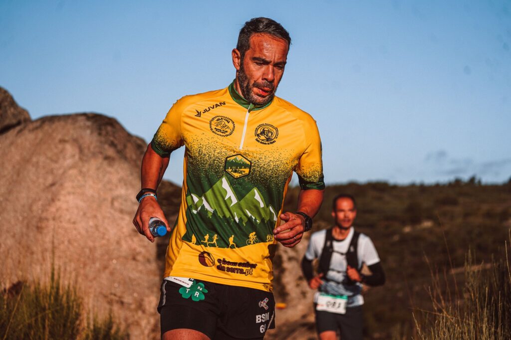 Focused athlete in colorful jersey running a trail marathon in scenic mountain setting.