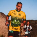 Focused athlete in colorful jersey running a trail marathon in scenic mountain setting.