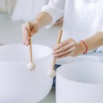 Hands playing crystal singing bowls with mallets, highlighting sound healing practice indoors.