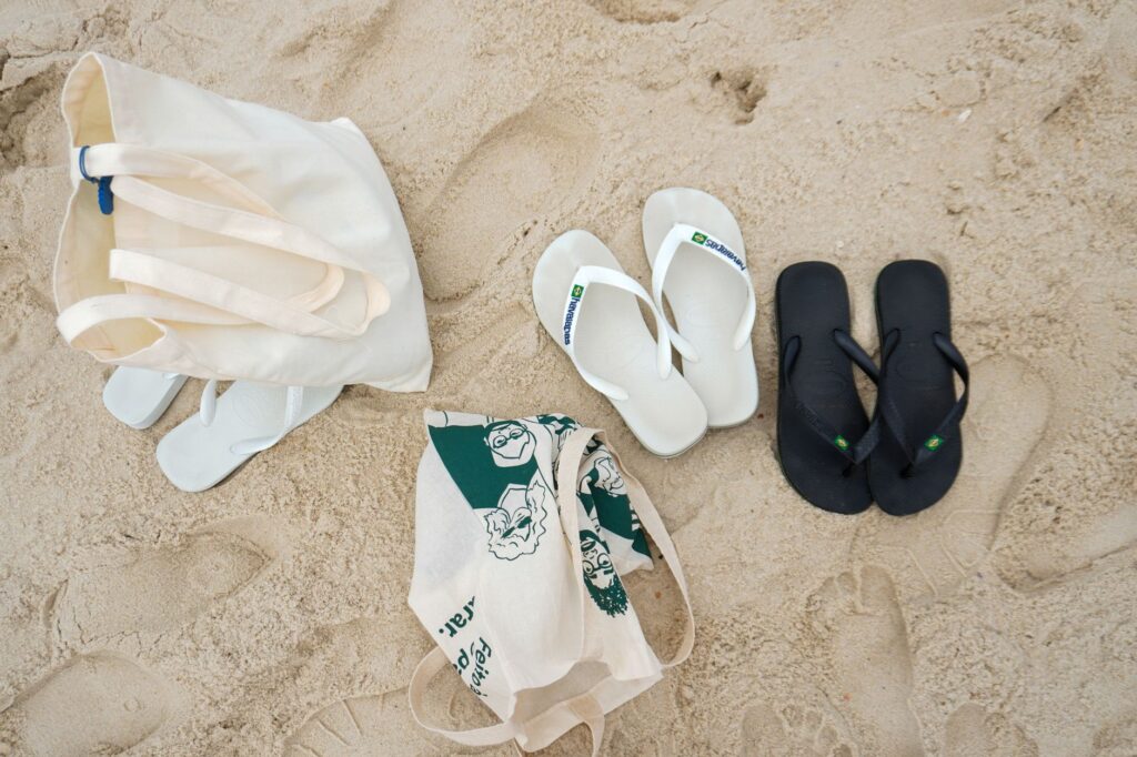 Flat lay of sandals and a tote bag on a sandy beach, ideal for summer themes.