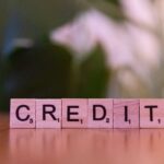 Close-up of wooden blocks spelling 'credit' with a blurred leafy background.